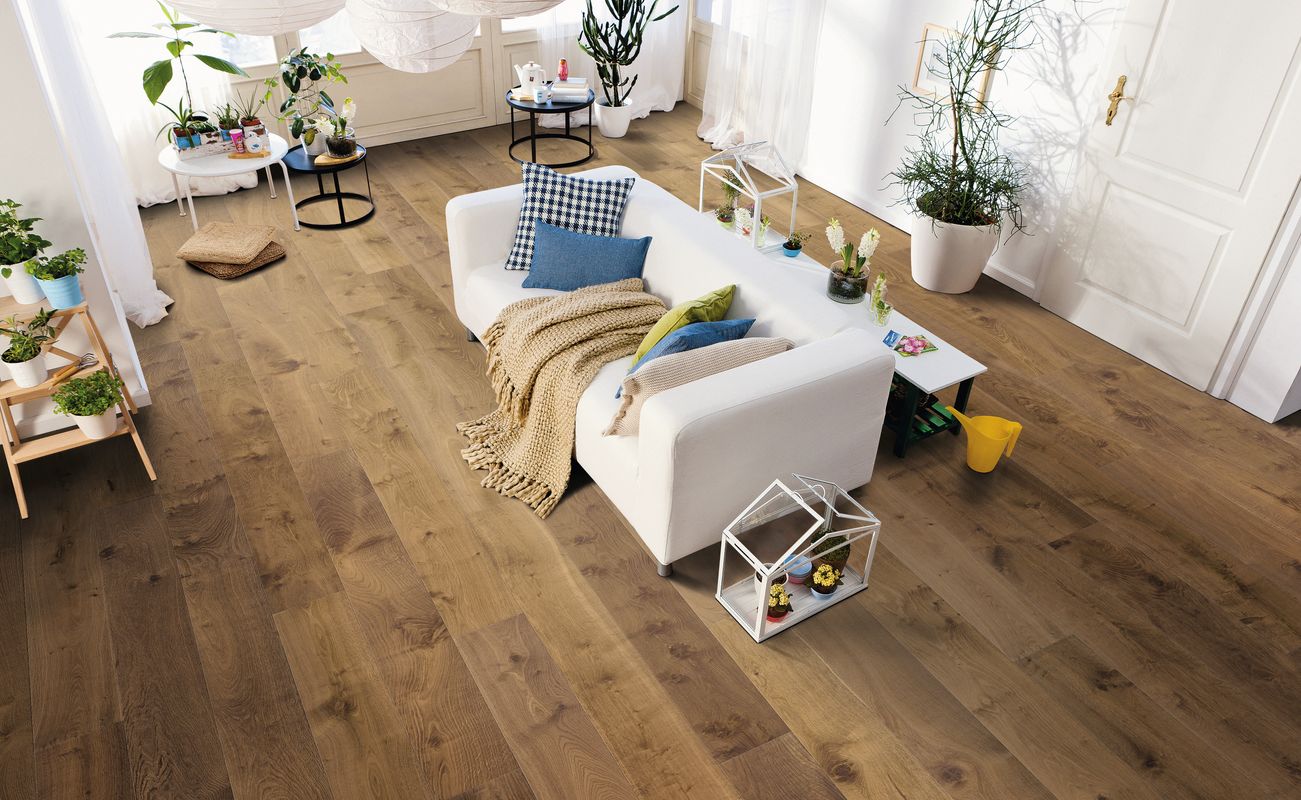 Heller Wohnraum mit einem weißen Sofa, einem Holzboden und Pflanzen. Auf dem Tisch stehen Dekorationen und ein paar Kissen auf dem Sofa.