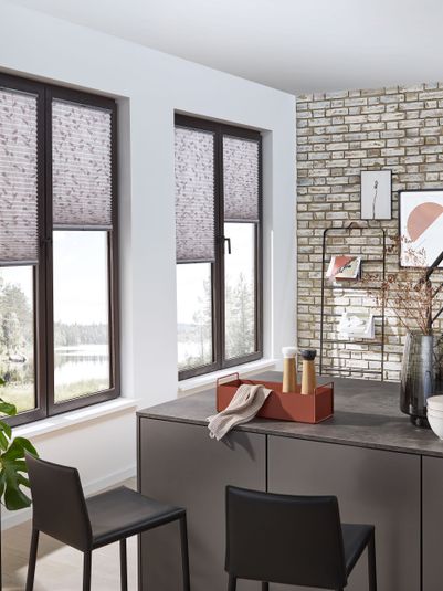 Moderne Wohnküche mit zwei Fenstern, dekorativen Rollos, einer Steinwand und einem Tisch mit Stühlen. Pflanzen und Deko-Elemente sind sichtbar.